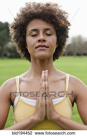 Stock Image - Mixed race woman practicing yoga in park. Fotosearch