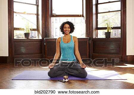 Stock Image - Mixed race woman practicing yoga in living room. Fotosearch