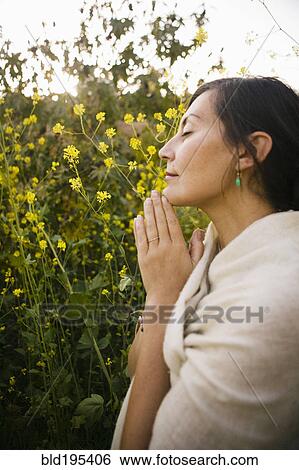 Stock Photograph - Mixed race woman praying with eyes closed in field. Fotosearch