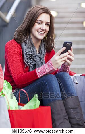 Stock Photograph - Mixed race woman shopping and text messaging on cell phone. Fotosearch