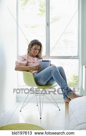 Mixed race woman sitting in chair using digital tablet View Large Photo Image Stock Image - Mixed race woman sitting in chair using digital tablet. Fotosearch