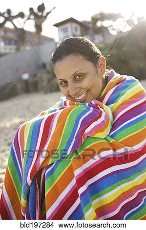 Picture - Mixed race woman sitting on beach wrapped in towel. Fotosearch
