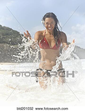 Stock Image - Mixed race woman splashing water on beach. Fotosearch