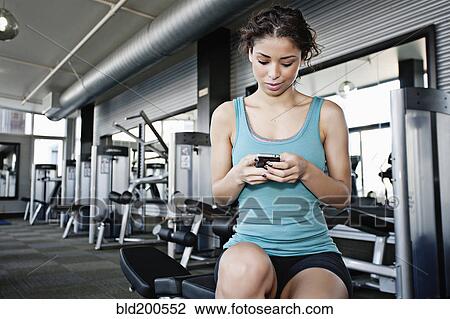 Mixed race woman text messaging on cell phone in health club View Large Photo Image Stock Image - Mixed race woman text messaging on cell phone in health club. Fotosearch