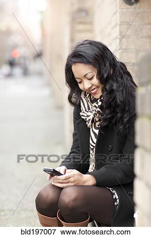 Stock Photo - Mixed race woman text messaging on cell phone. Fotosearch