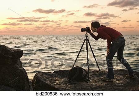 Stock Photograph - Mixed race woman using camera near ocean. Fotosearch