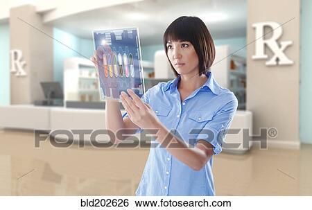Stock Photograph - Mixed race woman using digital tablet in pharmacy. Fotosearch