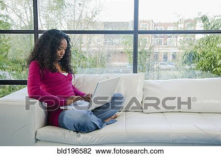 Stock Image - Mixed race woman using laptop on sofa. Fotosearch