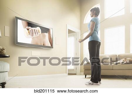 Stock Photography - Mixed race woman watching exercise program on television. Fotosearch