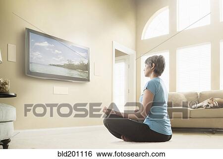 Stock Photograph - Mixed race woman watching meditation program on television. Fotosearch