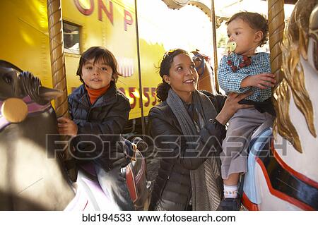 Stock Image - Mother and children enjoying carousel ride. Fotosearch
