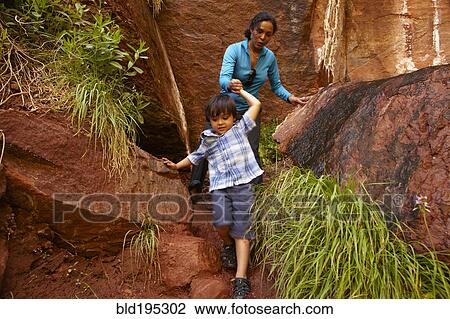 Stock Image - Mother helping son climb down rocks. Fotosearch