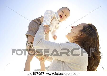 Stock Photo - Mother lifting baby outdoors. Fotosearch