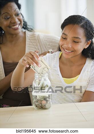 Mother watching daughter put money into jar View Large Photo Image Stock Photography - Mother watching daughter put money into jar. Fotosearch