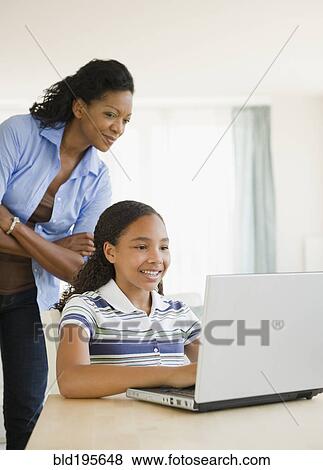 Stock Photo - Mother watching daughter using laptop. Fotosearch