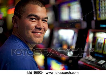 Picture - Native American man playing slot machine in casino. Fotosearch