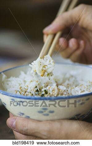 Stock Photo - Person eating bowl of rice with chopsticks. Fotosearch