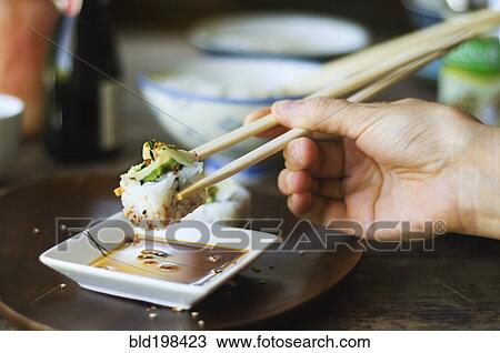 Stock Image - Person eating sushi with chopsticks. Fotosearch