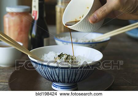 Picture - Person pouring sauce over bowl of rice. Fotosearch