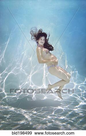 Stock Photo - Pregnant Caucasian woman swimming underwater. Fotosearch