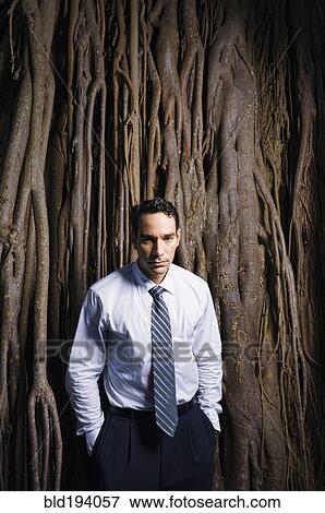 Stock Photo - Sad Latin businessman standing near tree roots. Fotosearch