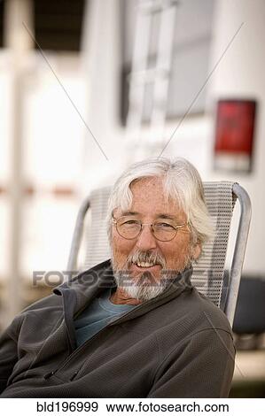 Stock Photo - Senior Caucasian man sitting outside motor home. Fotosearch