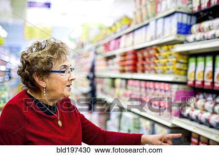 Stock Image - Senior Hispanic woman shopping in grocery store. Fotosearch