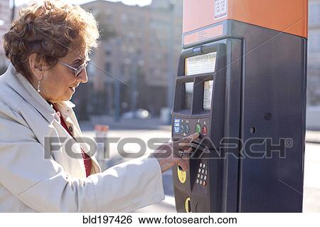 Stock Photograph - Senior Hispanic woman using parking meter. Fotosearch