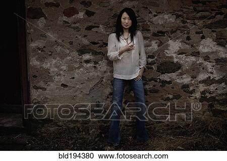 Stock Image - Serious Asian woman leaning against wall. Fotosearch