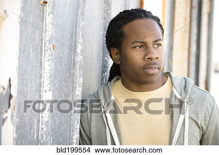 Picture - Serious Black man leaning against wall. Fotosearch