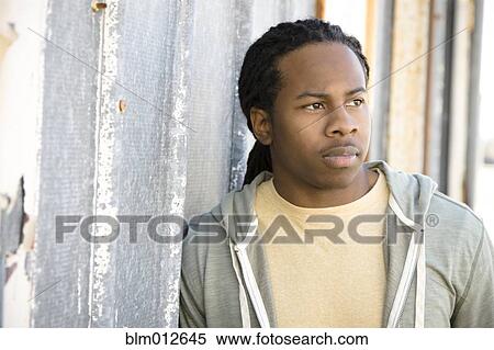 Stock Photography - Serious Black man leaning against wall. Fotosearch