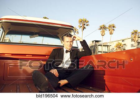Picture - Serious Caucasian man sitting in tuxedo in back of truck. Fotosearch