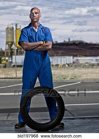 Serious mechanic standing with tire View Large Photo Image Stock Photo - Serious mechanic standing with tire. Fotosearch