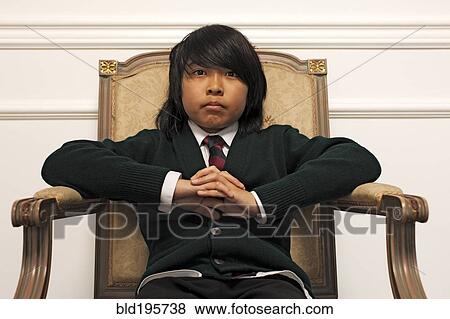 Stock Photo - Serious Vietnamese boy sitting on elegant chair. Fotosearch