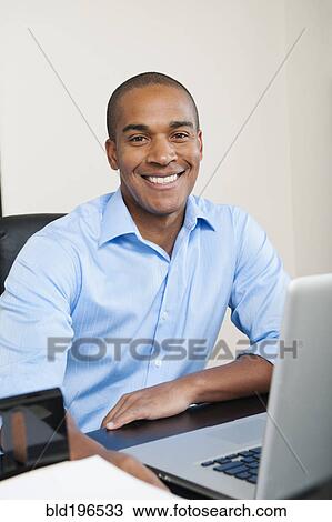 Smiling African American businessman sitting at desk View Large Photo Image Stock Image - Smiling African American businessman sitting at desk. Fotosearch