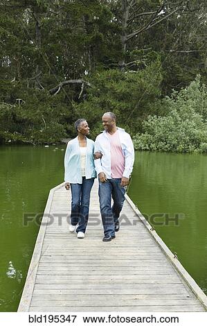 Stock Photo - Smiling African American couple standing on pier at lake. Fotosearch