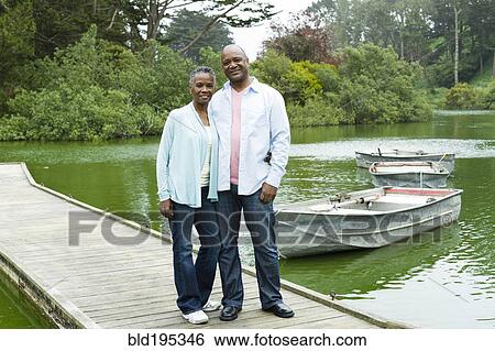 Stock Photograph - Smiling African American couple standing on pier at lake. Fotosearch