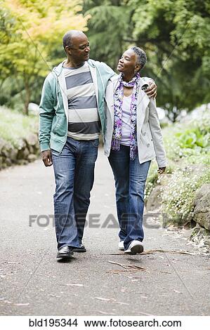 Picture - Smiling African American couple walking in park. Fotosearch