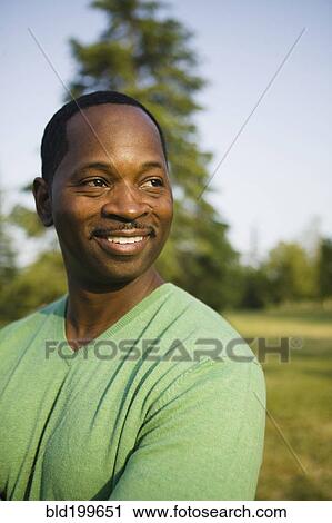 Smiling African American man standing in park View Large Photo Image Stock Image - Smiling African American man standing in park. Fotosearch