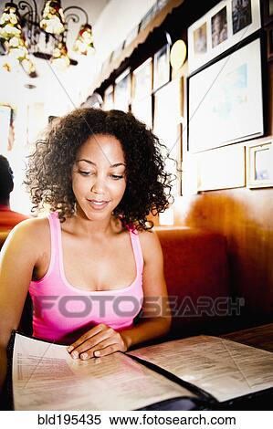 Stock Photography - Smiling African American woman reading menu in diner. Fotosearch