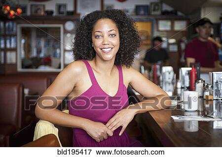 Stock Photo - Smiling African American woman sitting at diner counter. Fotosearch