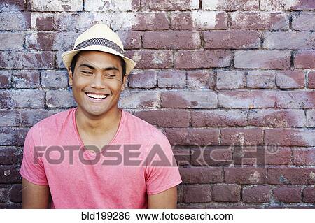 Stock Photograph - Smiling Asian man near brick wall. Fotosearch