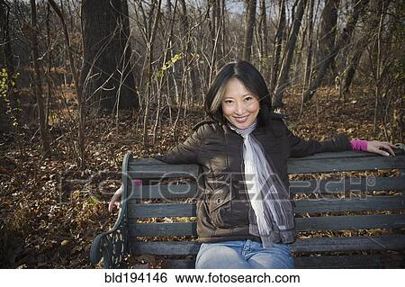 Smiling Asian woman sitting on park bench View Large Photo Image Stock Photograph - Smiling Asian woman sitting on park bench. Fotosearch