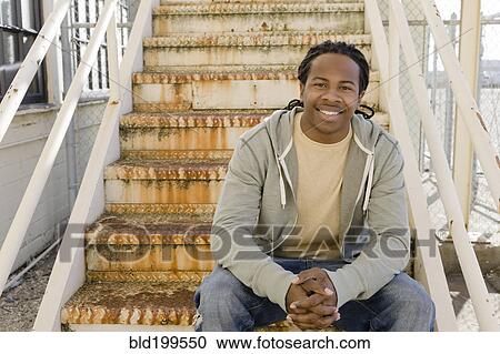 Stock Image - Smiling Black man sitting on staircase. Fotosearch