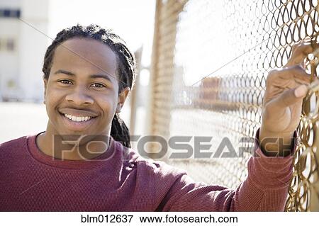 Smiling Black man standing near fence View Large Photo Image Stock Photo - Smiling Black man standing near fence. Fotosearch