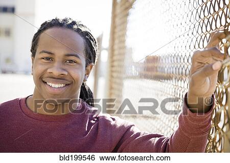 Smiling Black man standing near fence View Large Photo Image Stock Photograph - Smiling Black man standing near fence. Fotosearch