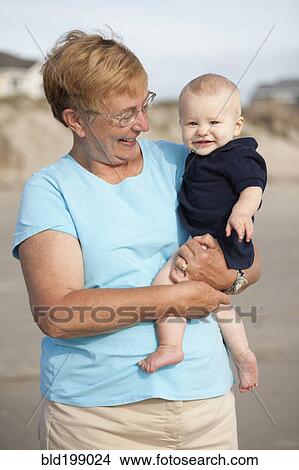 Picture - Smiling Caucasian grandmother holding grandson on beach. Fotosearch