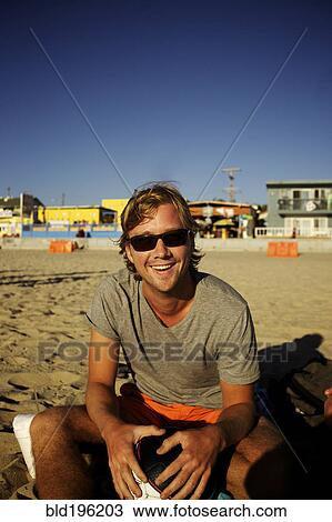 Stock Image - Smiling Caucasian man sitting on beach. Fotosearch