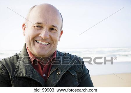 Stock Image - Smiling Caucasian man standing on beach. Fotosearch