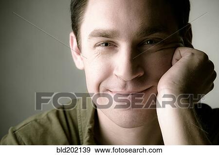 Stock Photo - Smiling Caucasian man with head in hands. Fotosearch
